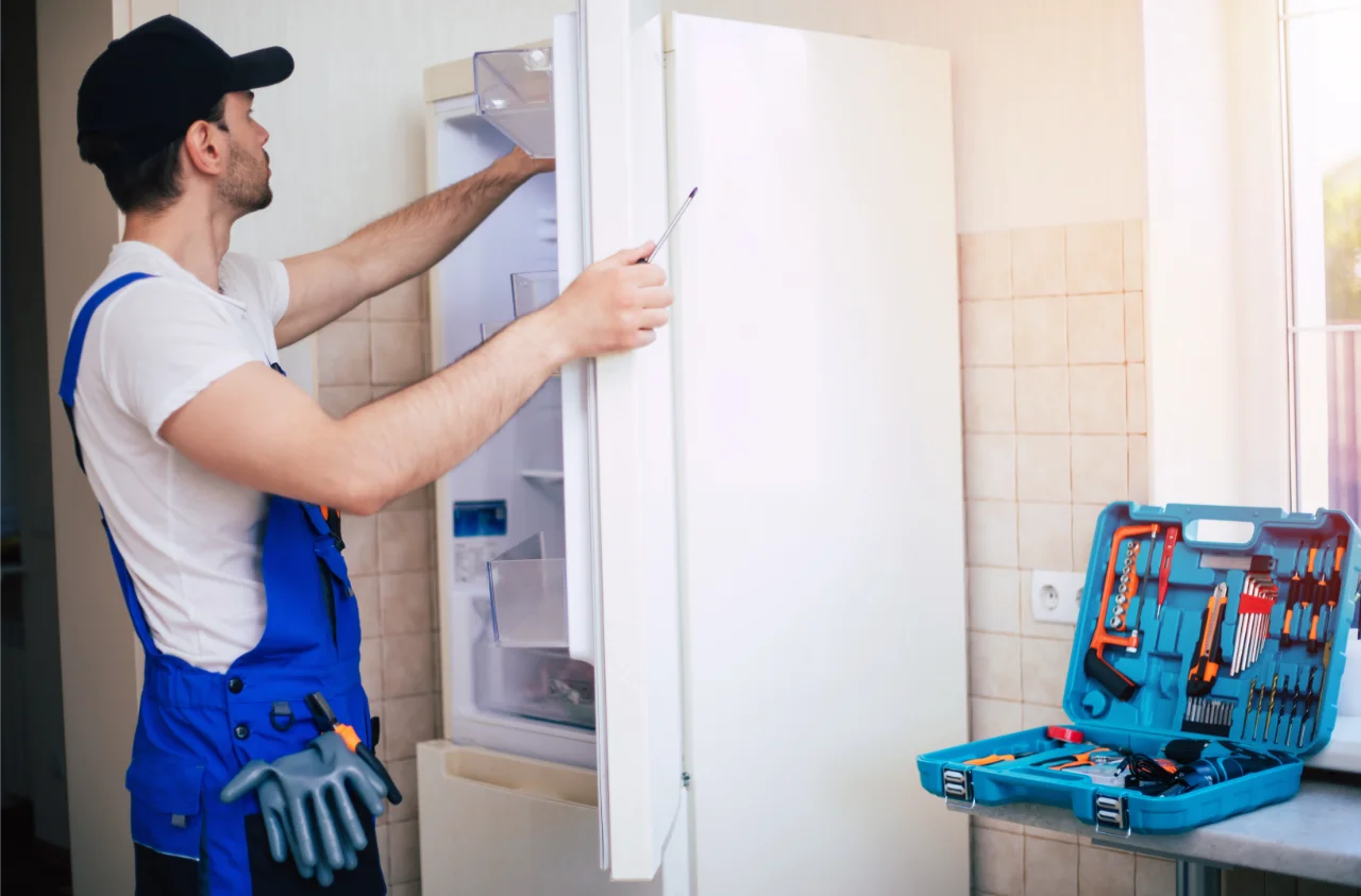 professional young repairman worker uniform cap with modern toolbox with equipment is repairing refrigerator kitchen
